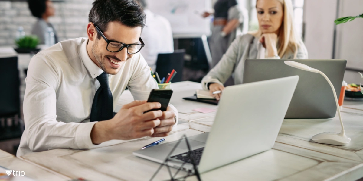 Man using phone next to other employee in front of desktops