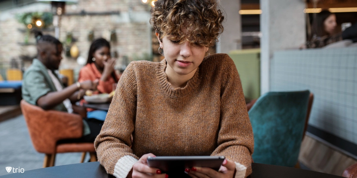 Woman looking at tablet in a coffeeshop with two people sitting behind her