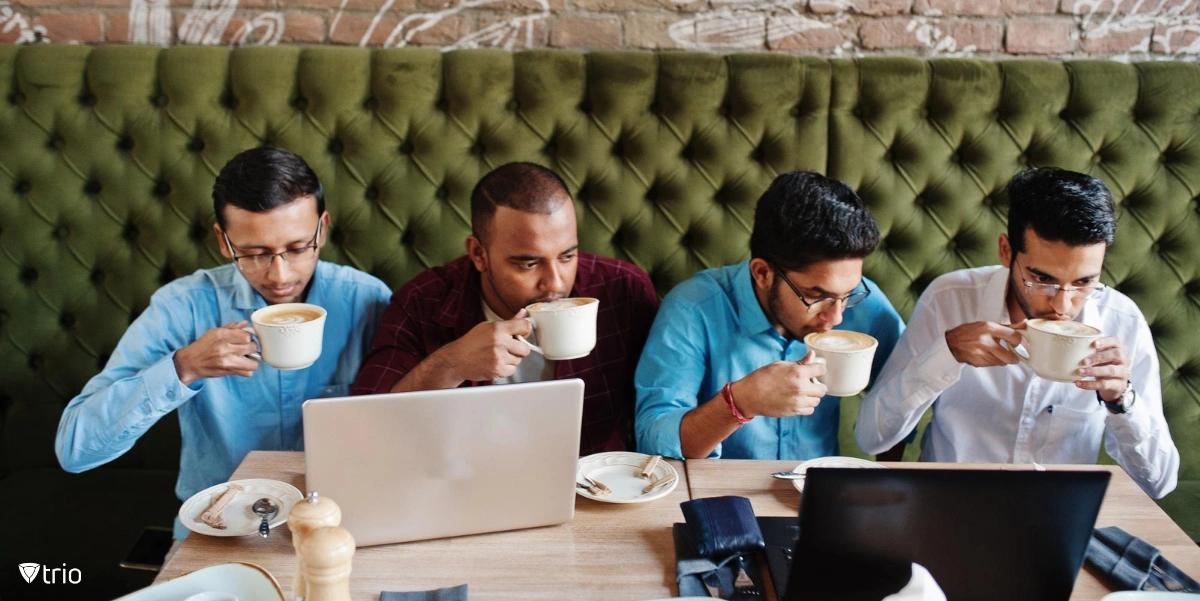 Four men sipping coffee while working with laptops at a cafe