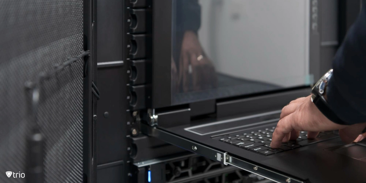 A person typing on a laptop with some computer servers in the background