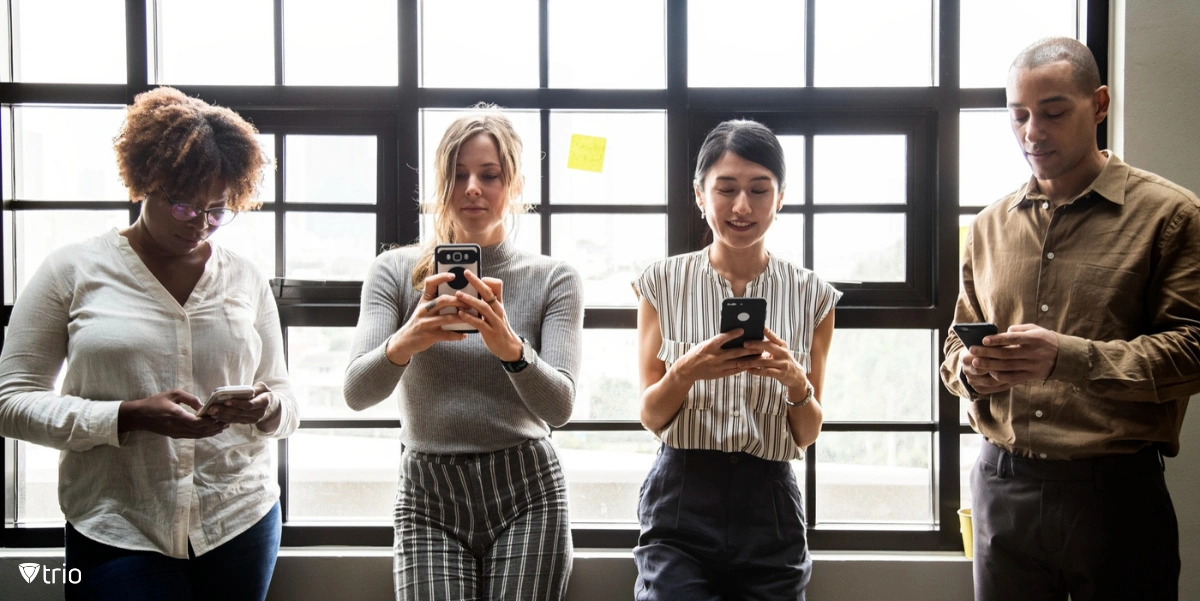 Four employees using mobile devices in an office while standing next to a phone