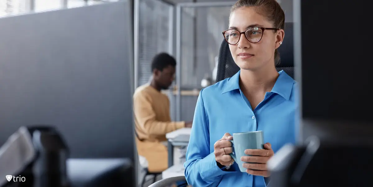 Employee in office in front of two monitors with mug in hand