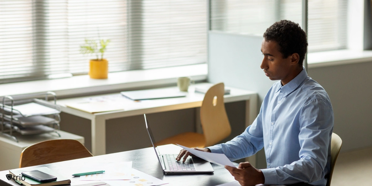 Employee holding sheet and using software on laptop in office