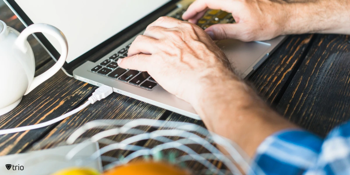Eine Nahaufnahme der Hand eines Mannes, der an einem Holzschreibtisch auf einem Laptop tippt und Softwarebereitstellungen auf einigen Geräten testet, bevor sie unternehmensweit ausgerollt werden, um eine reibungslose, fehlerfreie Implementierung sicherzustellen.