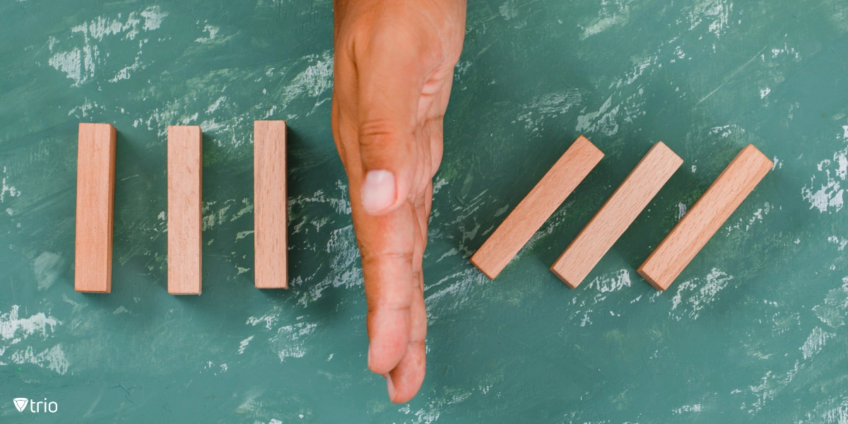 Eine Hand, die als Barriere zwischen herabfallenden Holzklötzen fungiert und das Konzept der Risikominimierung symbolisiert.