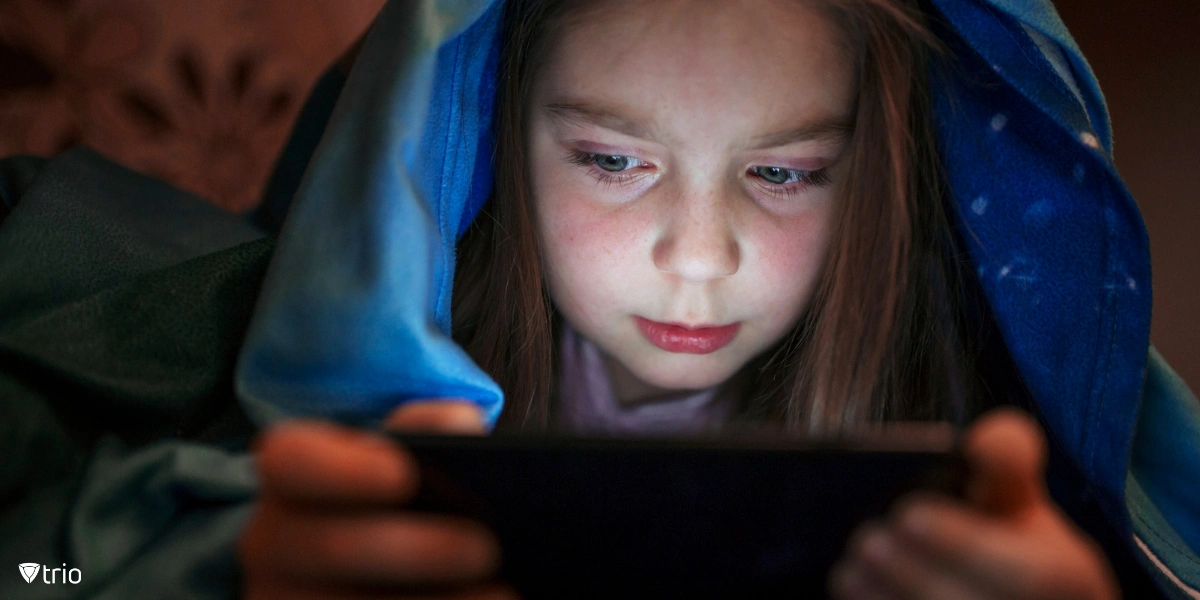 Kleines Mädchen, das über ein Telefon mit der Hülle auf dem Kopf soziale Medien betrachtet