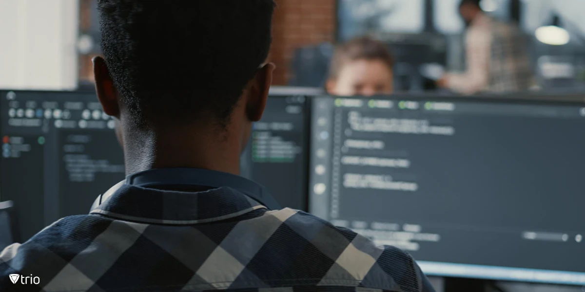 Porträt eines Programmierers mit Laptop, der an einem Schreibtisch sitzt und auf mehreren Bildschirmen Code analysiert