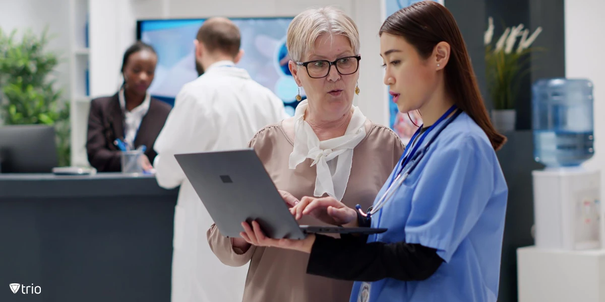 Seniorin und medizinische Fachangestellte mit einem Laptop bei der Beratung an der Krankenhausrezeption