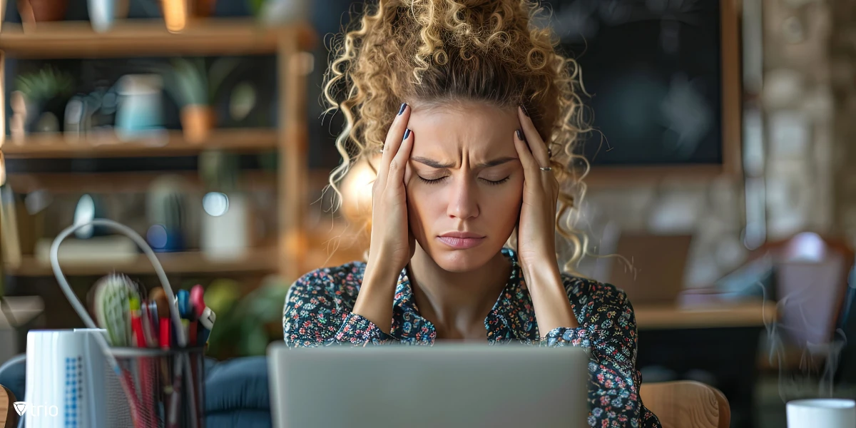überforderte Frau mit den Händen in den Haaren, die vor einem Laptop sitzt