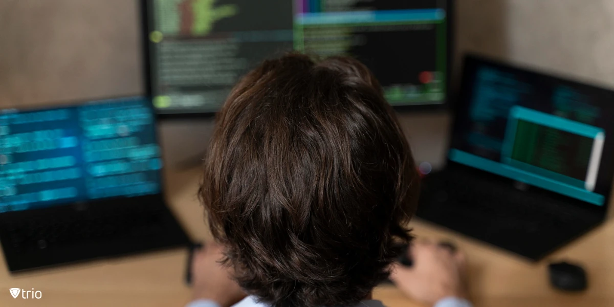 A programmer is focused on coding at a desk with multiple screens displaying lines of code.