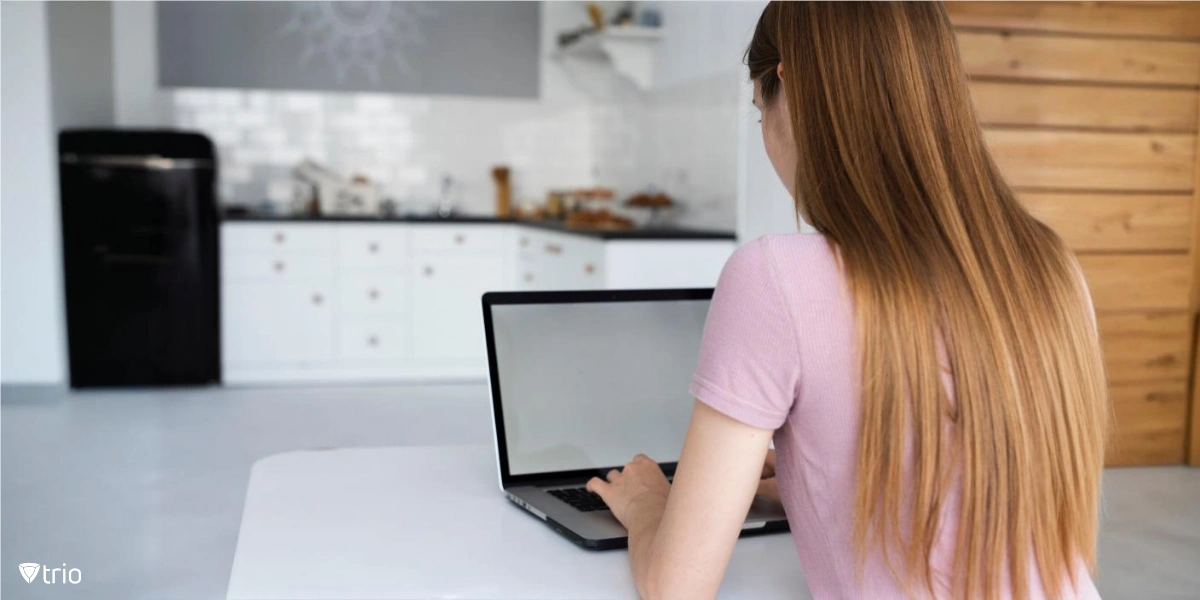 Eine Person sitzt an einem Tisch in einer Küche und benutzt einen Laptop