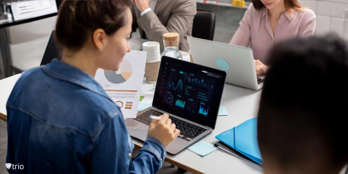 A modern office environment where a  woman is seated at a table, analyzing data on her laptop screen.