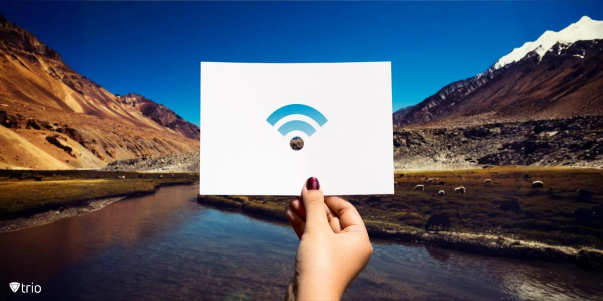 Eine Hand hält ein Stück perforiertes Papier mit einem ausgeschnittenen Wi-Fi-Symbol vor einer atemberaubenden Naturlandschaft mit Bergen und einem Fluss.