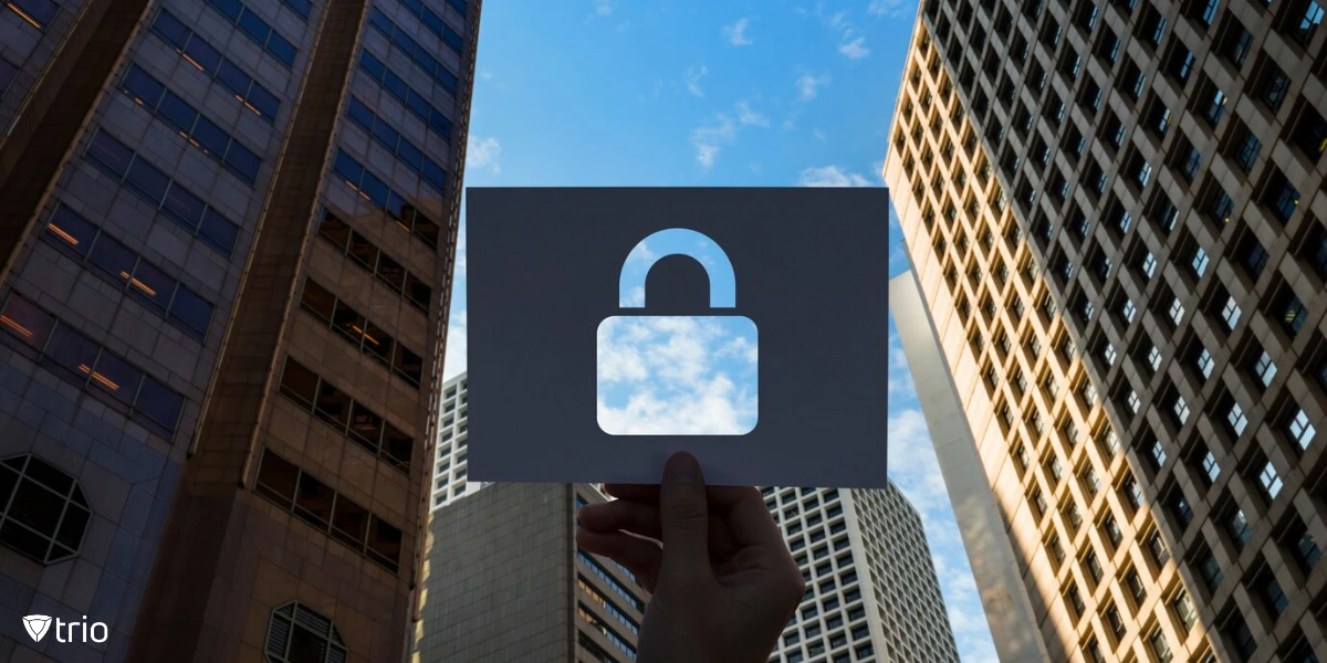 A dark-colored piece of paper with a cutout of a padlock symbol, held up against a backdrop of tall skyscrapers and a bright blue sky.