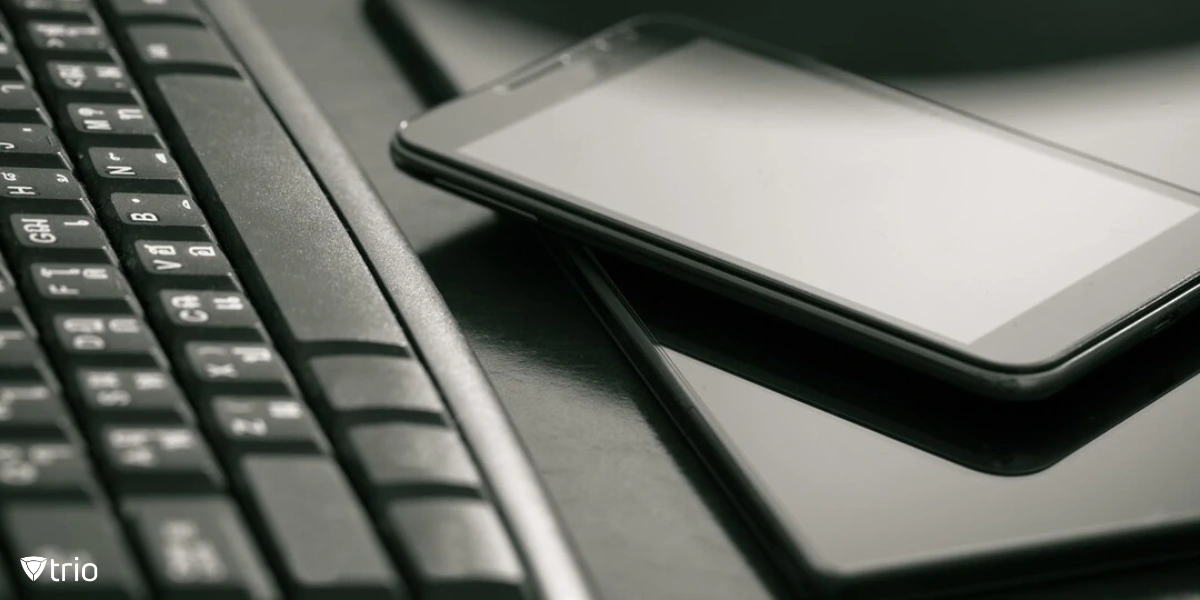 A monochrome close-up shot showing a smartphone and a tablet stacked beside a traditional desktop keyboard.
