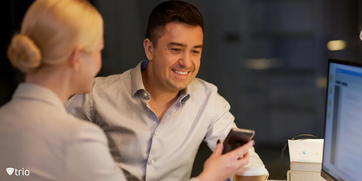 Two coworkers distracted by social media on their smartphones in an office environment.