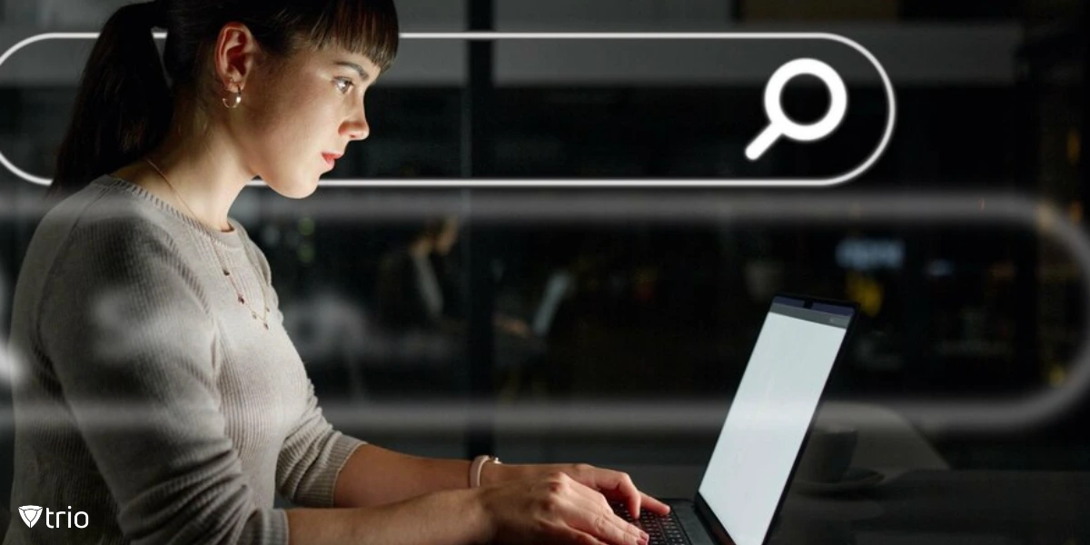 A woman typing in the search bar on her laptop in a dark office room.