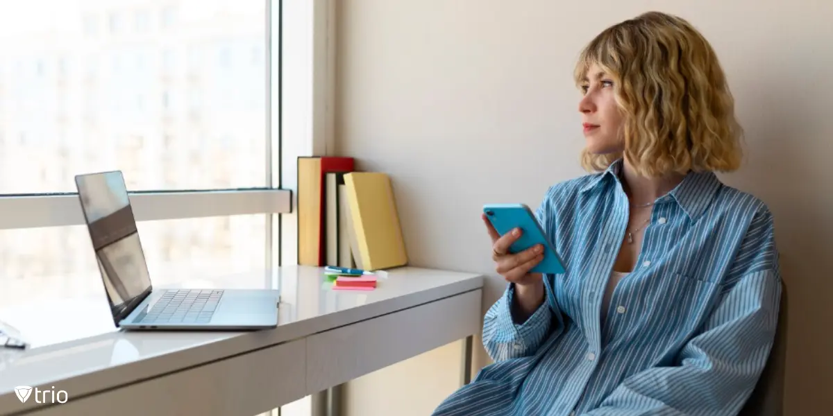 A woman holding a smartphone at work while looking outside.